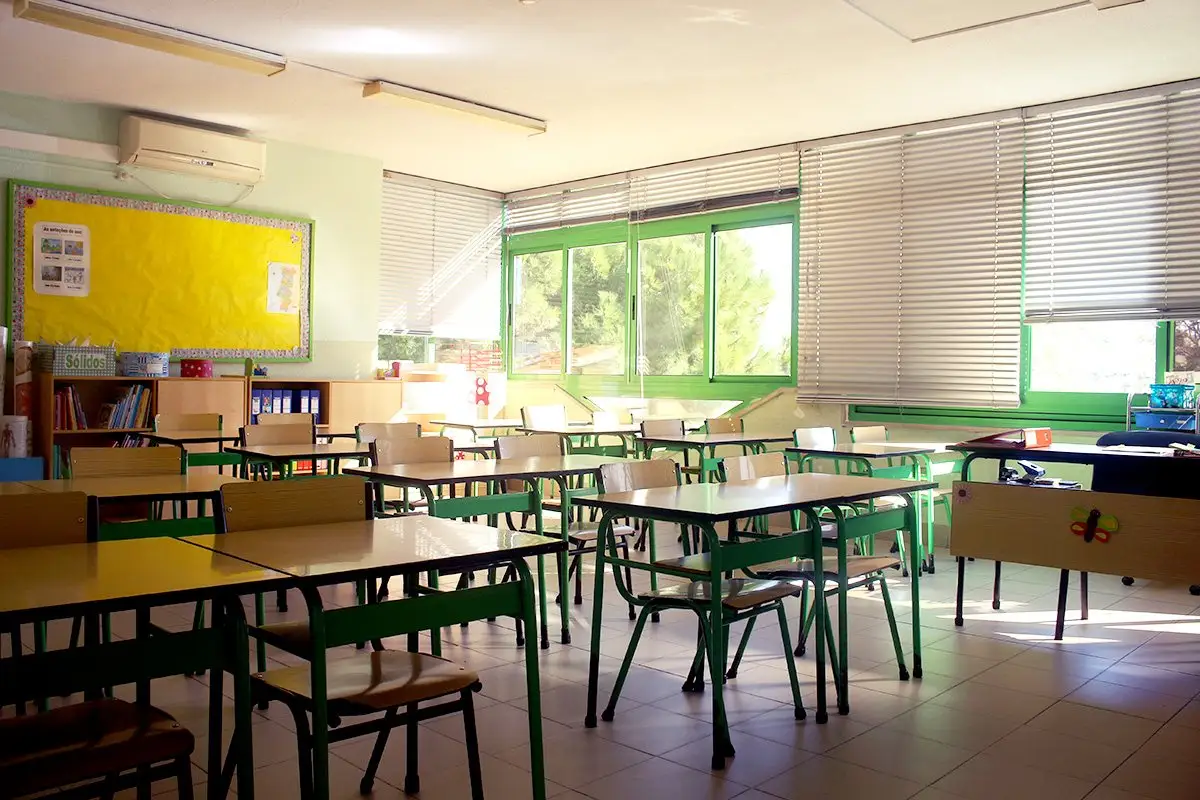 An empty, sunlit classroom with green desks at Escola Nova Apostólica