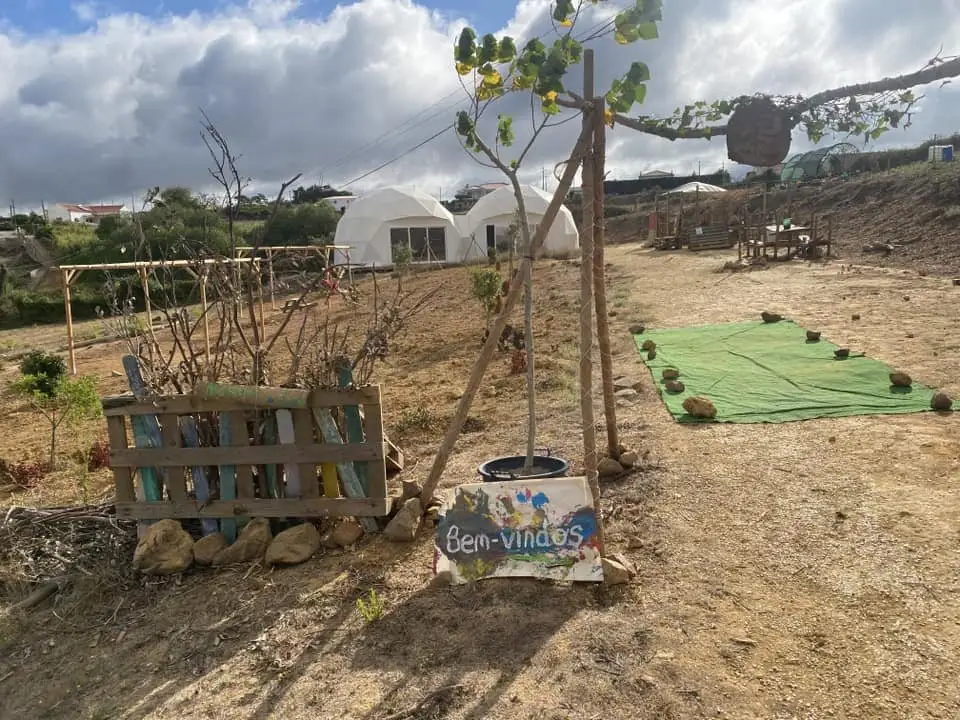 Outdoor learning area with a welcome sign, young trees and white dome tents at Bosque da Alegria