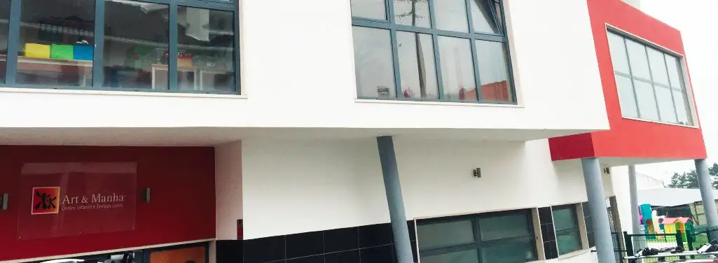 Outside of the Colégio Art & Manha building, with its red sign and upper-floor classroom windows