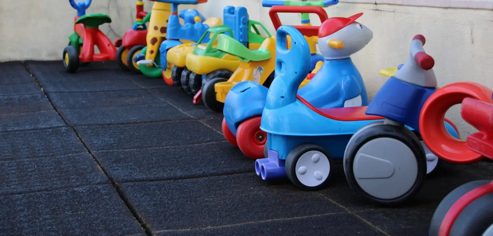 A row of children's ride-on toys and tricycles in the covered playground at Externato Florinda Leal