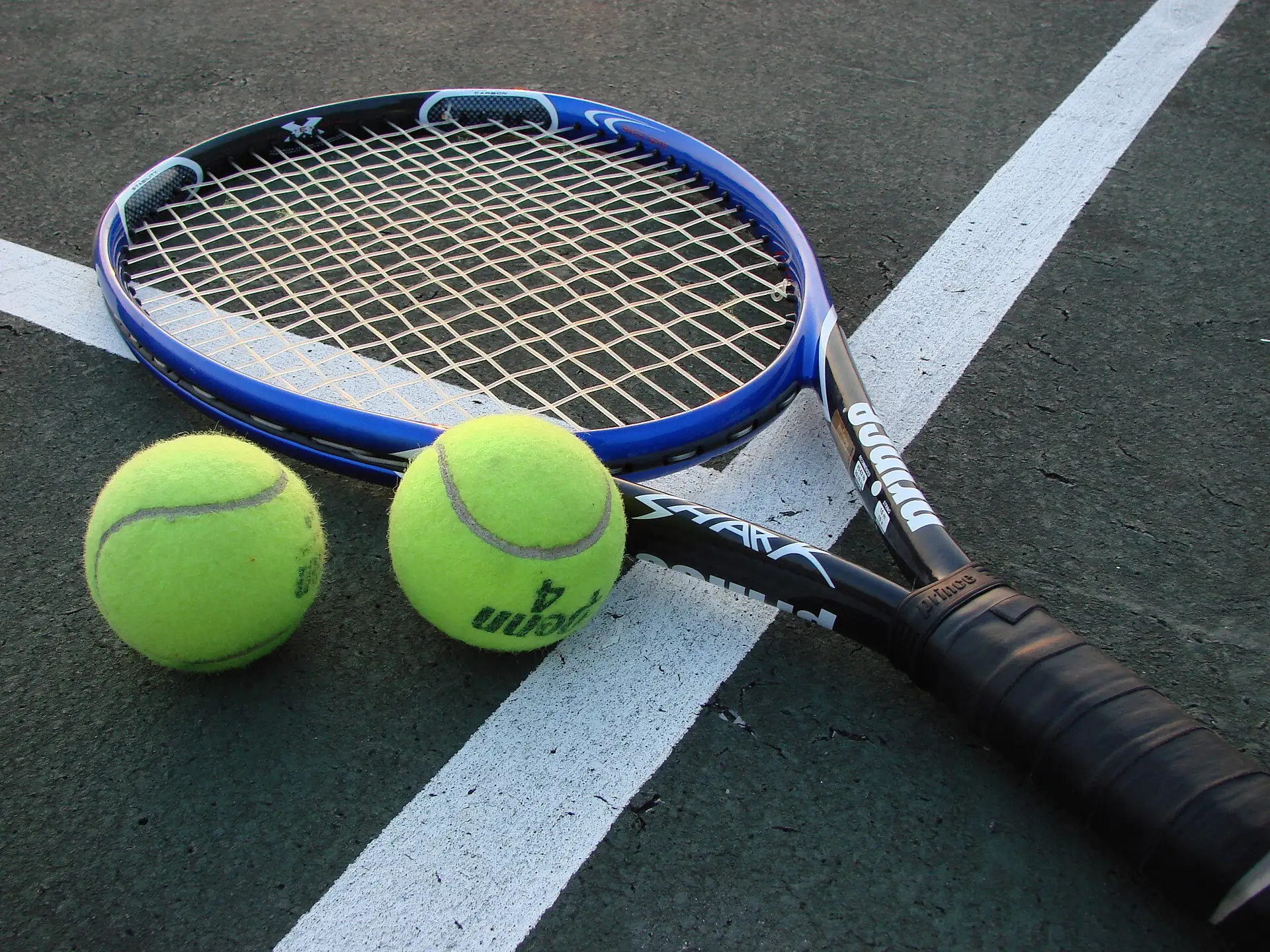 A tennis racket and two tennis balls on a hard court
