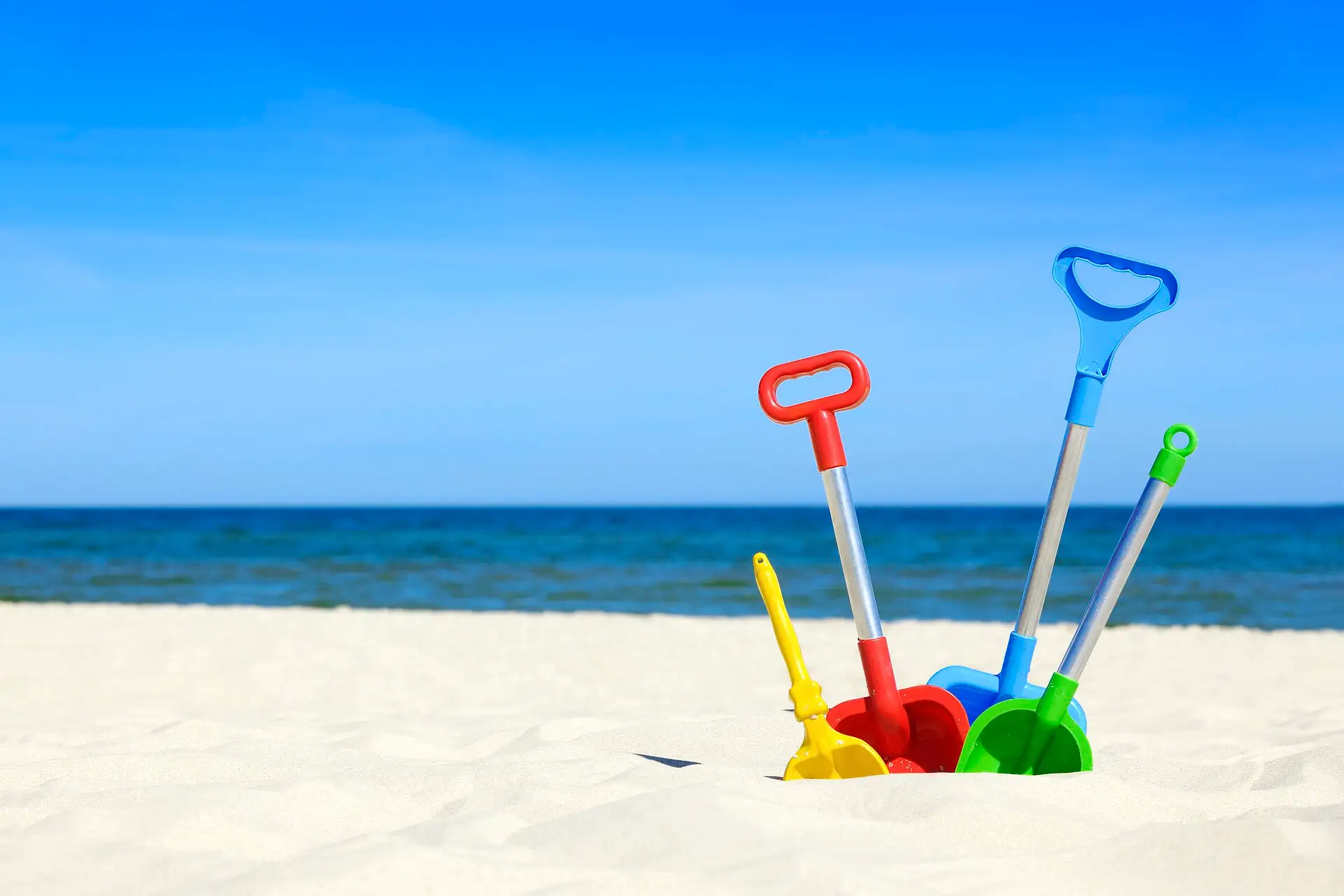 Colourful toy spades standing in the sand on a beach, with the sea behind