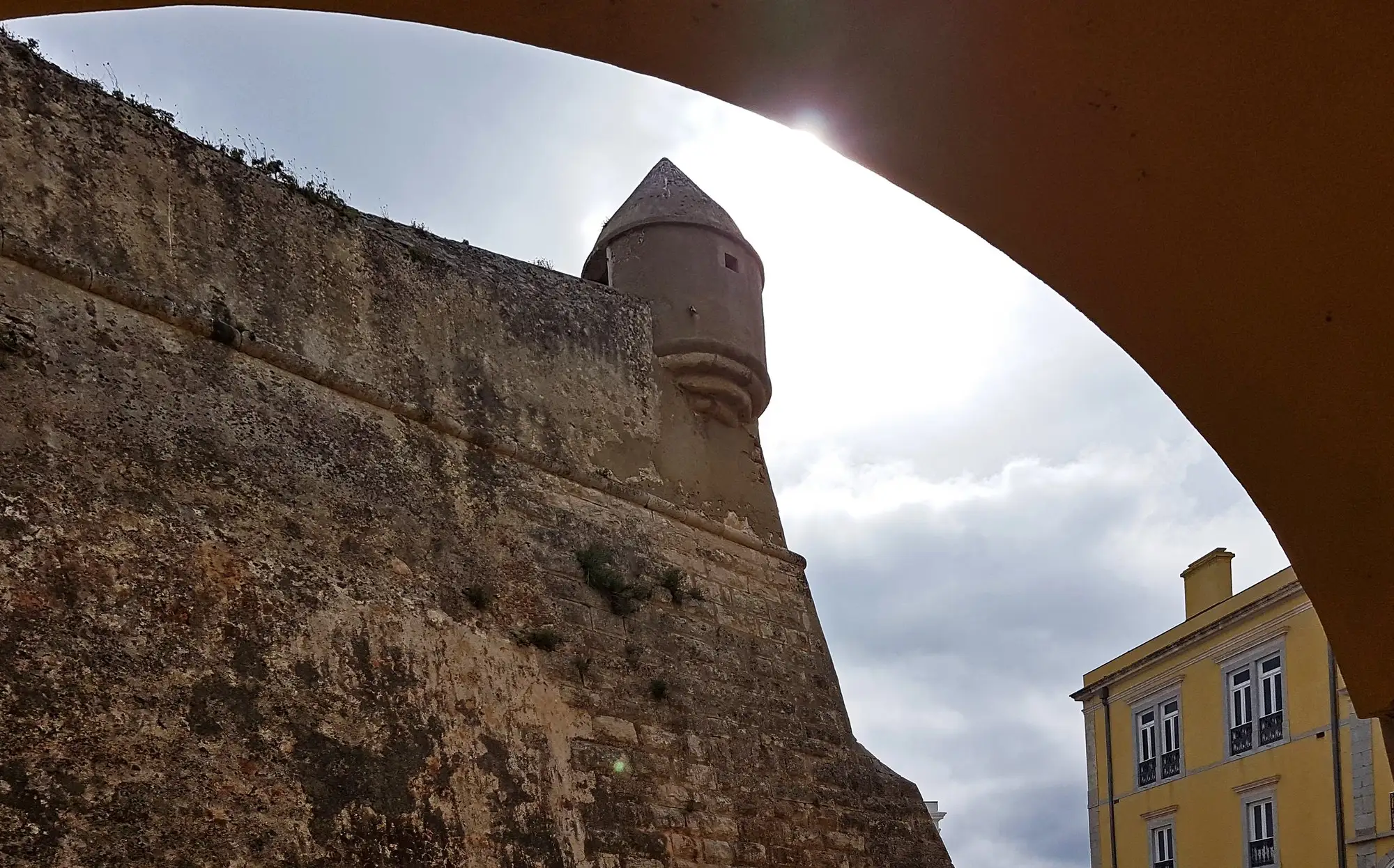 The old stone walls and watchtower of the Cidadela in Cascais, seen through an arch