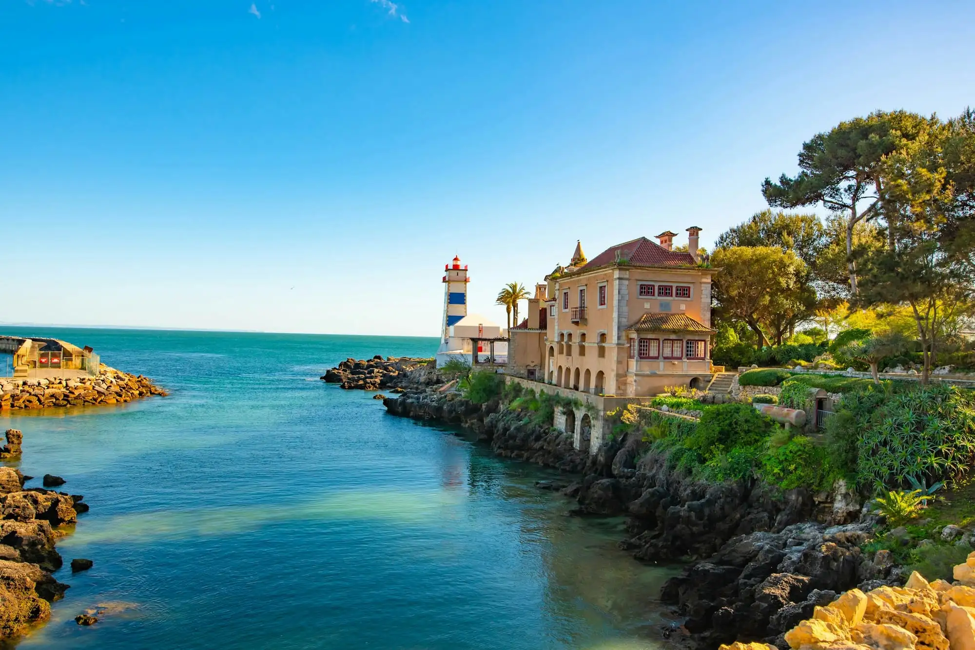 Santa Marta lighthouse and the rocky shoreline of Cascais under a clear blue sky