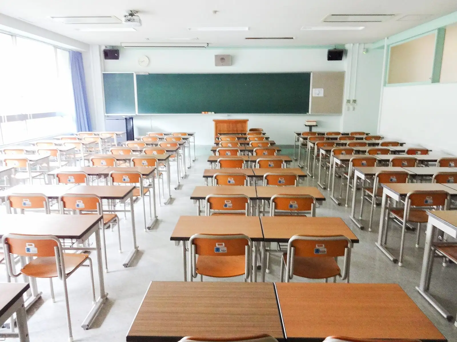 An empty classroom with rows of desks and chairs facing a blackboard